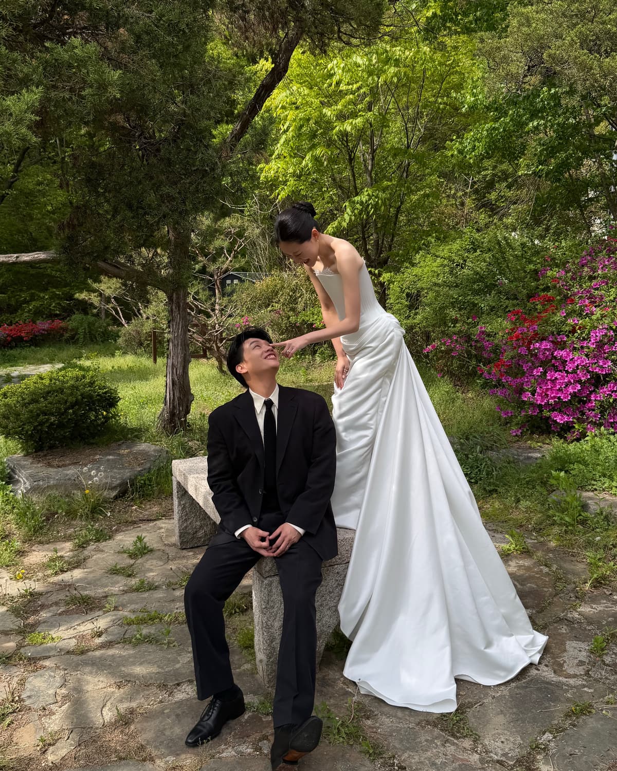 꽃과 나무가 있는 정원에서 서로를 바라보며 웨딩 스냅을 남기는 두 사람